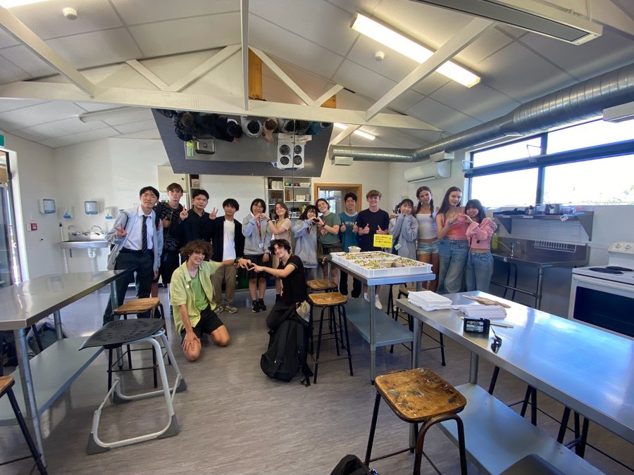Students laughing together during a cooking session in a New Zealand school kitchen.