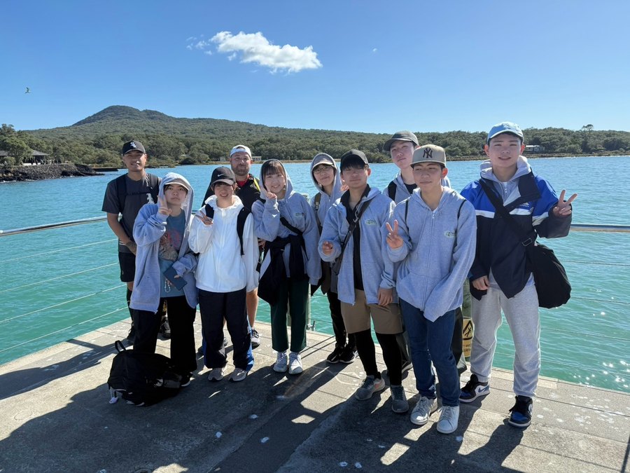 International students at an Auckland wharf with Rangitoto Island in the background.