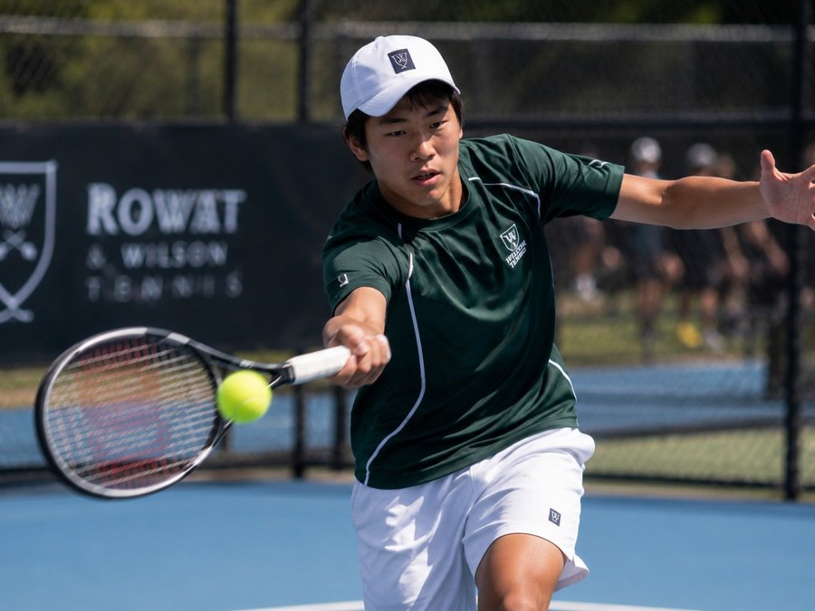 A tennis player mid-stride during a competitive match, eyes locked on the ball as the racket meets it.